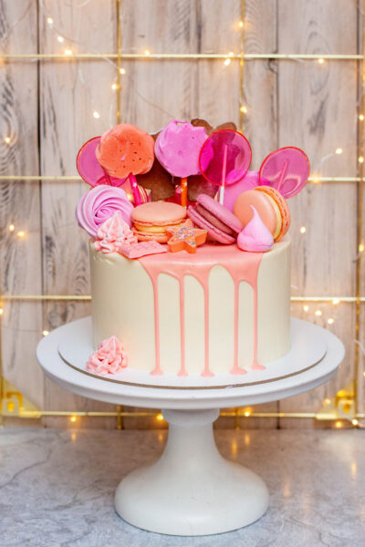 White cake with pink melted chocolate, meringues and lollipops on festive background